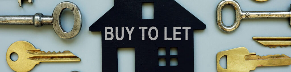 A black house shape key tag with BUY TO LET written in white. It is laying face up on a blue surface amongst some keys. 